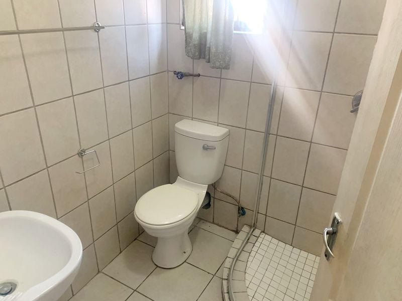 A compact bathroom featuring a toilet, shower cubicle, and washbasin with neutral ceramic tiling throughout.