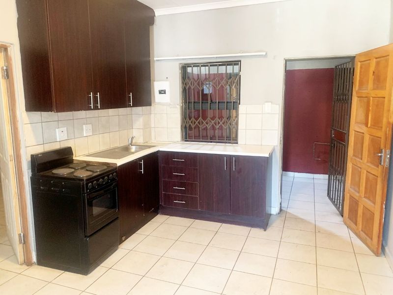A functional kitchen featuring dark wood cabinetry, tiled backsplash, and ceramic flooring, equipped with a built-in sink and security features on the window and door.