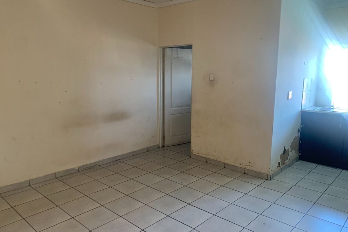 An empty open-plan living and kitchen area featuring tiled flooring, requiring cosmetic updates to the walls and finishes.