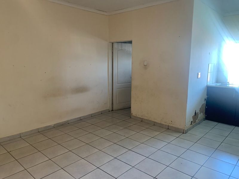 An empty open-plan living and kitchen area featuring tiled flooring, requiring cosmetic updates to the walls and finishes.