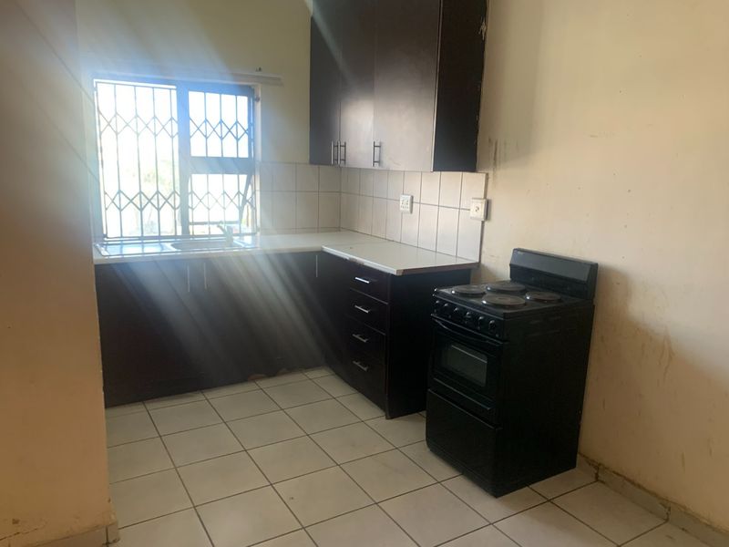 A functional kitchen featuring dark cabinetry, tiled flooring, and a freestanding stove, requiring cosmetic updates to the walls and cabinetry to improve its appeal.