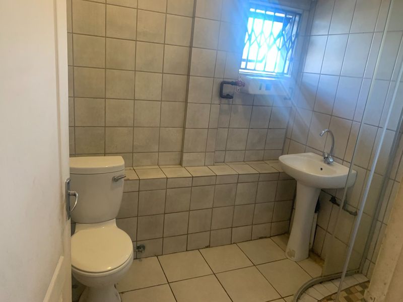 A functional bathroom featuring a pedestal basin, toilet, and tiled finishes, requiring some cosmetic updates to improve its overall condition and appeal.
