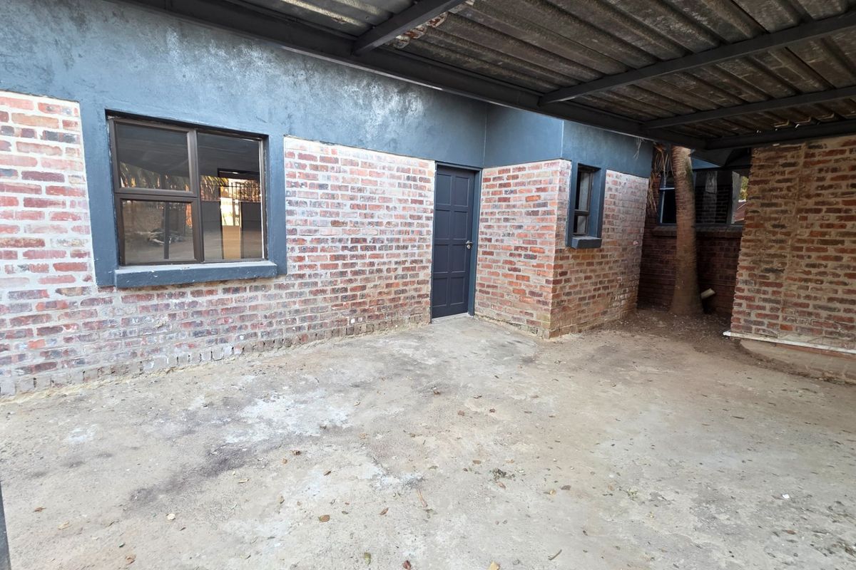 A rear exterior view of the townhouse featuring exposed brick walls, a covered patio area with concrete flooring, and aluminium window frames.