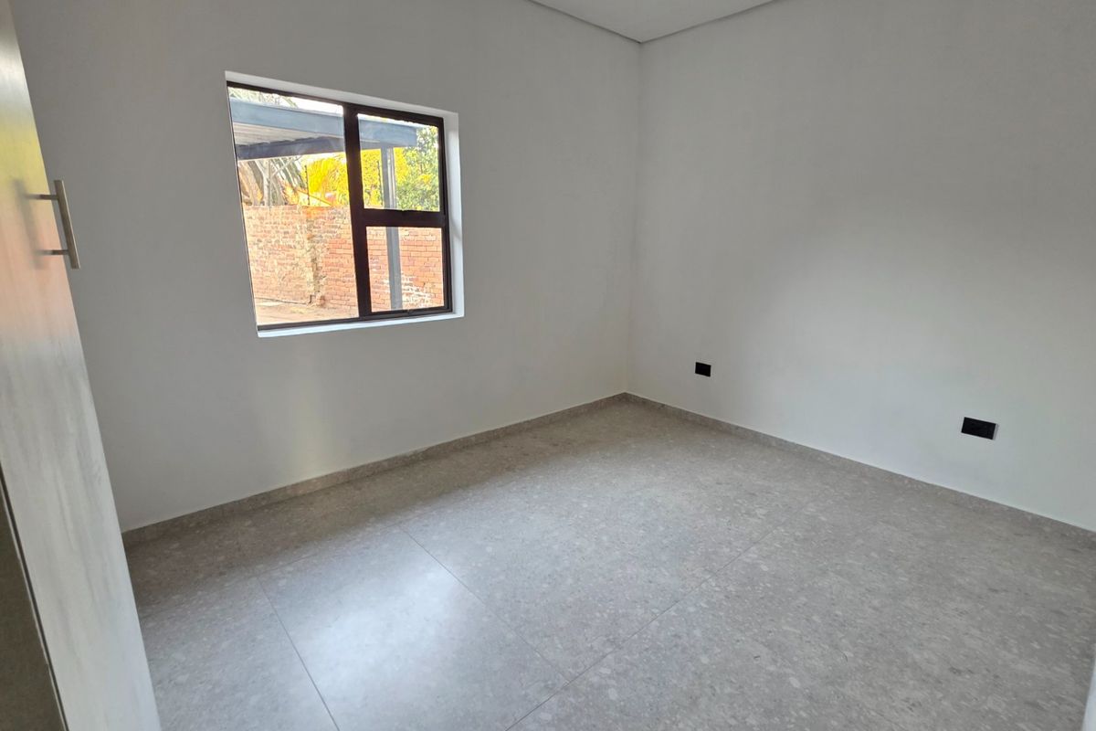 A clean, empty bedroom featuring neutral tiled flooring, a built-in cupboard, and a window providing natural light.