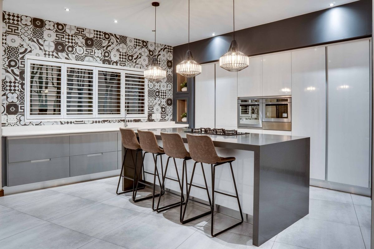 Modern kitchen featuring a large central island with stone countertops, built-in appliances, sleek cabinetry, and decorative patterned wall tiling.
