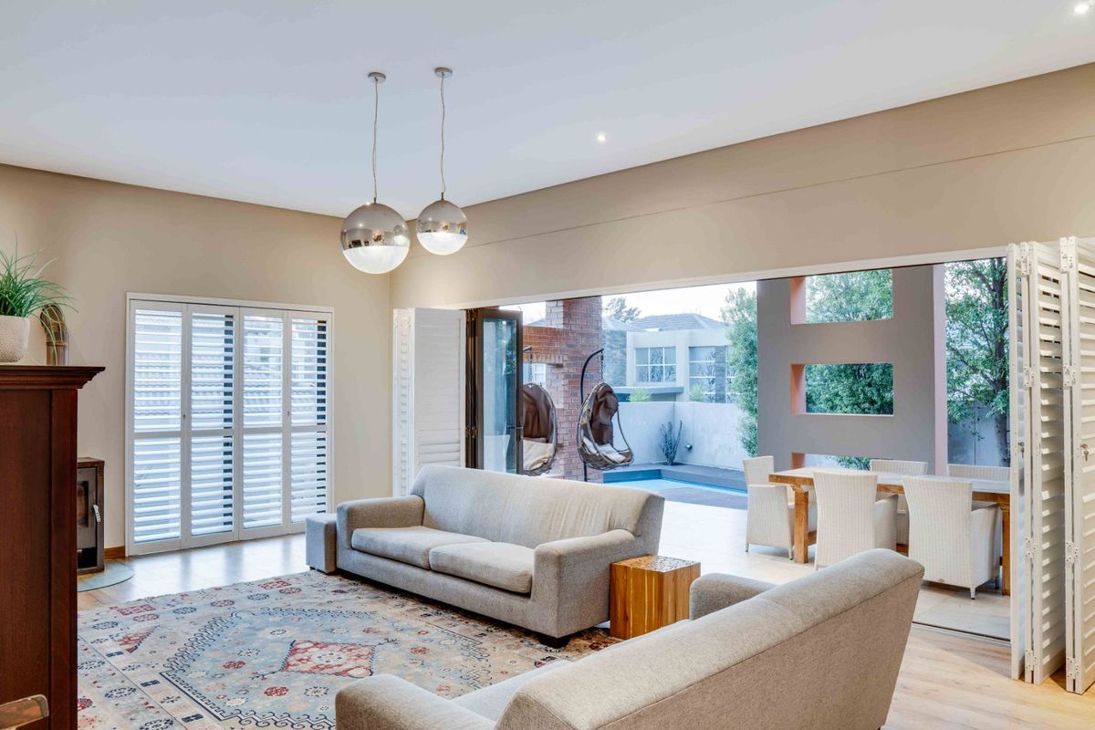 Spacious living room featuring a fireplace, plantation shutters, and large stacking doors that open seamlessly to the outdoor patio and pool area.