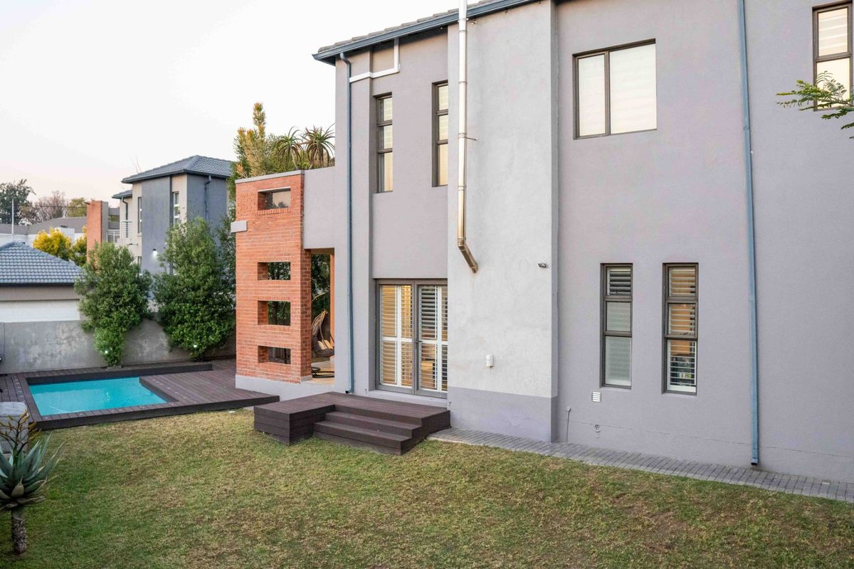 Rear view of a modern two-story home featuring a swimming pool, timber decking, and a distinctive brick architectural feature wall.