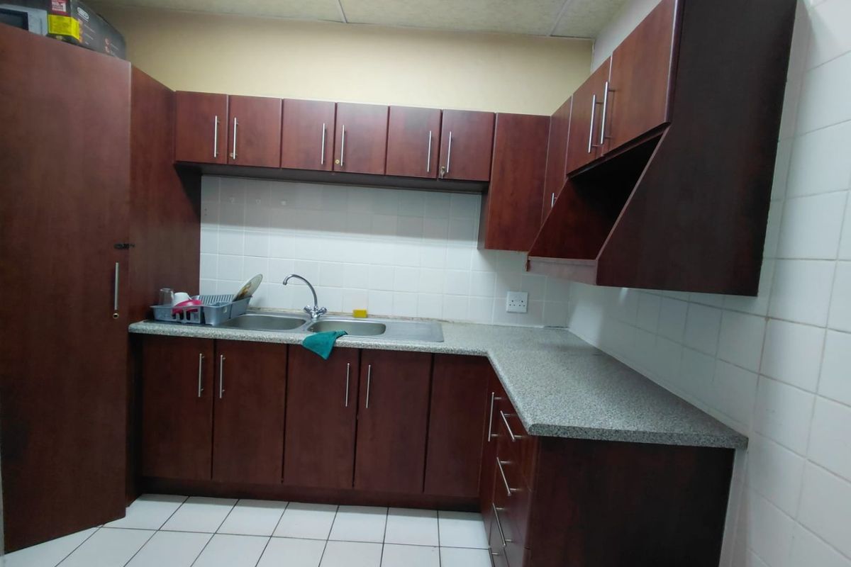A functional commercial kitchen area featuring dark wood cabinetry, granite-look laminate countertops, a double basin sink, and tiled finishes throughout.