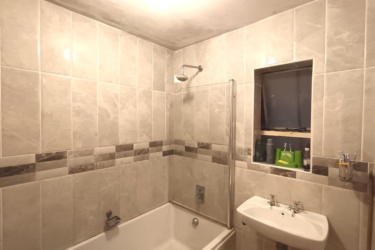 A functional bathroom featuring a bathtub with a glass shower screen, wall-mounted basin, and neutral wall tiling.