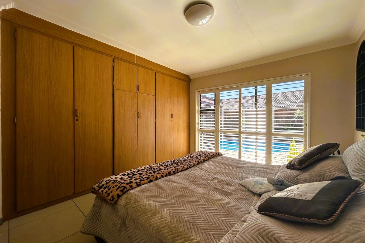A bedroom featuring extensive built-in wooden cupboards, tiled flooring, and security shutters overlooking the pool area.