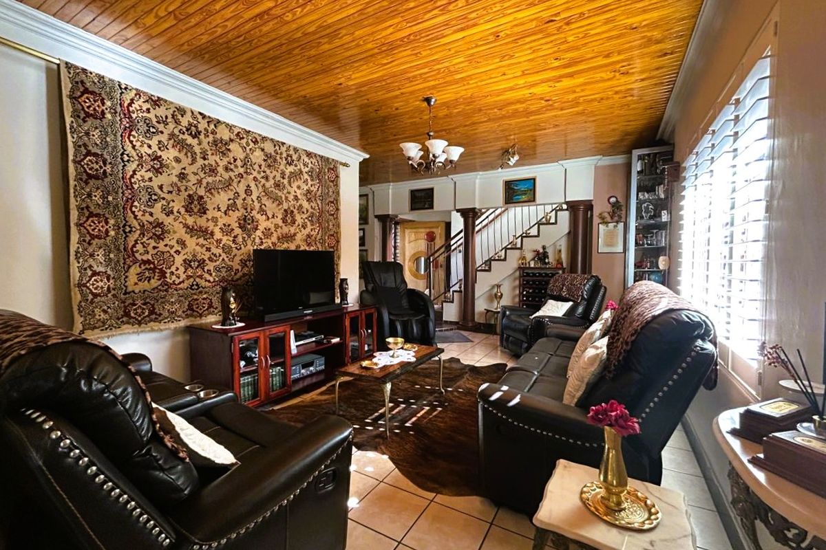 A living room featuring a distinctive timber-clad ceiling, ceramic tiled flooring, and a staircase with a wooden balustrade, complemented by plantation shutters.