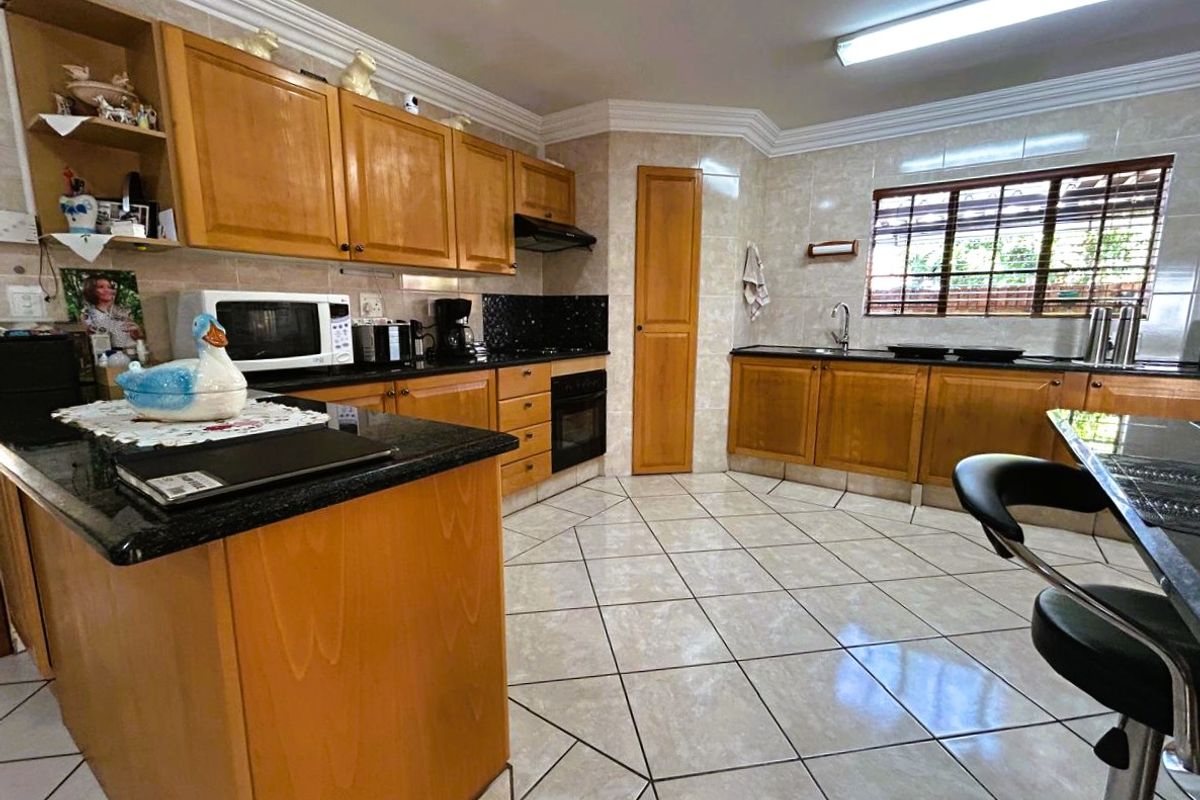 Spacious kitchen featuring wooden cabinetry, granite countertops, built-in oven, extractor fan, and tiled flooring with a functional layout.