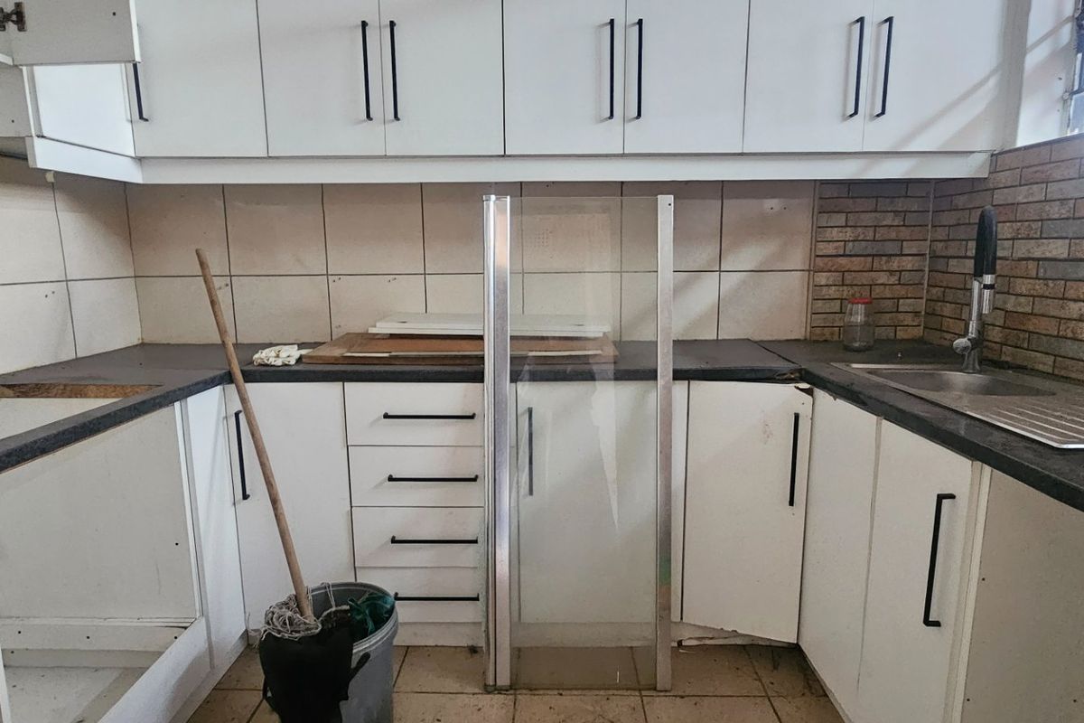 A functional kitchen space featuring white cabinetry, tiled backsplash, and a stainless steel sink, currently requiring minor repairs and cosmetic updates.