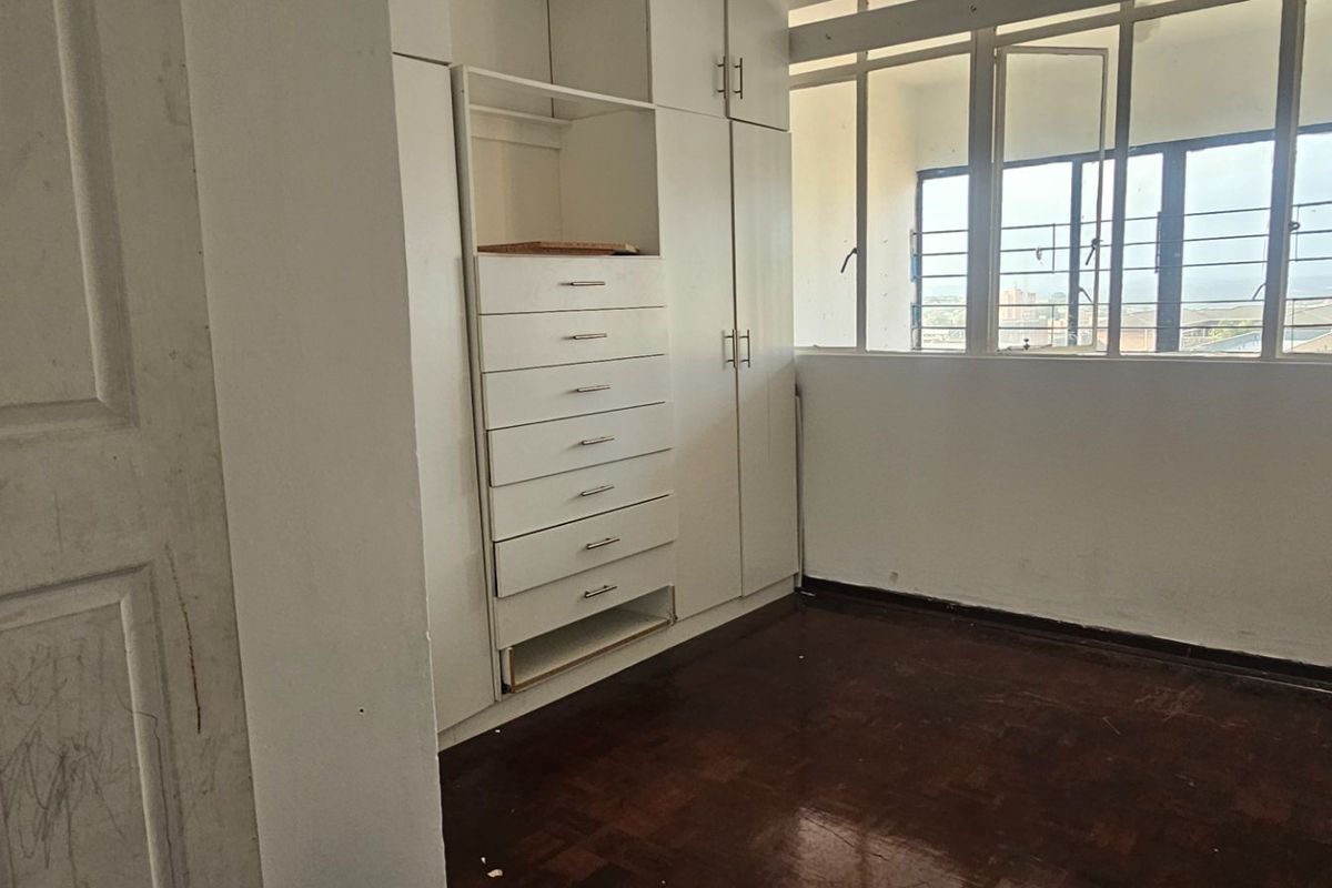 A vacant bedroom featuring built-in cupboards, parquet flooring, and a large window with security bars, offering a blank canvas for potential updates.