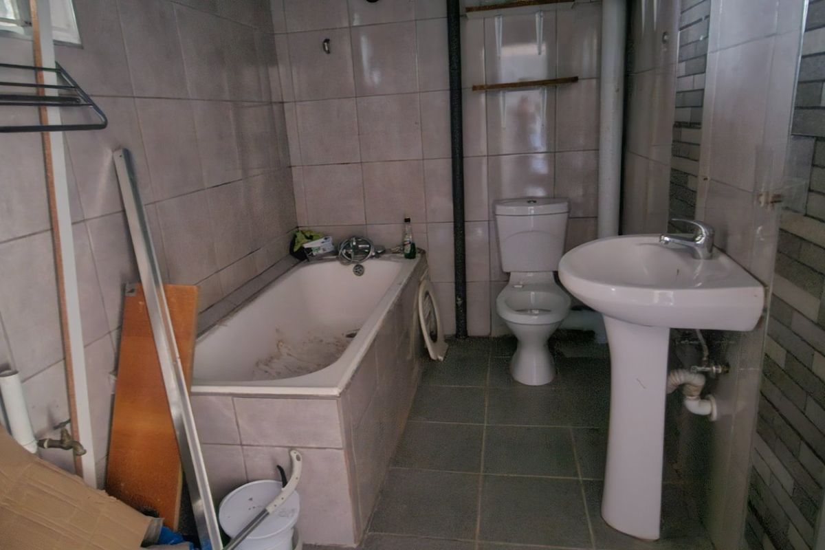A dated bathroom featuring a bathtub, pedestal sink, and toilet with tiled finishes, requiring cosmetic updates and maintenance to improve its overall condition.