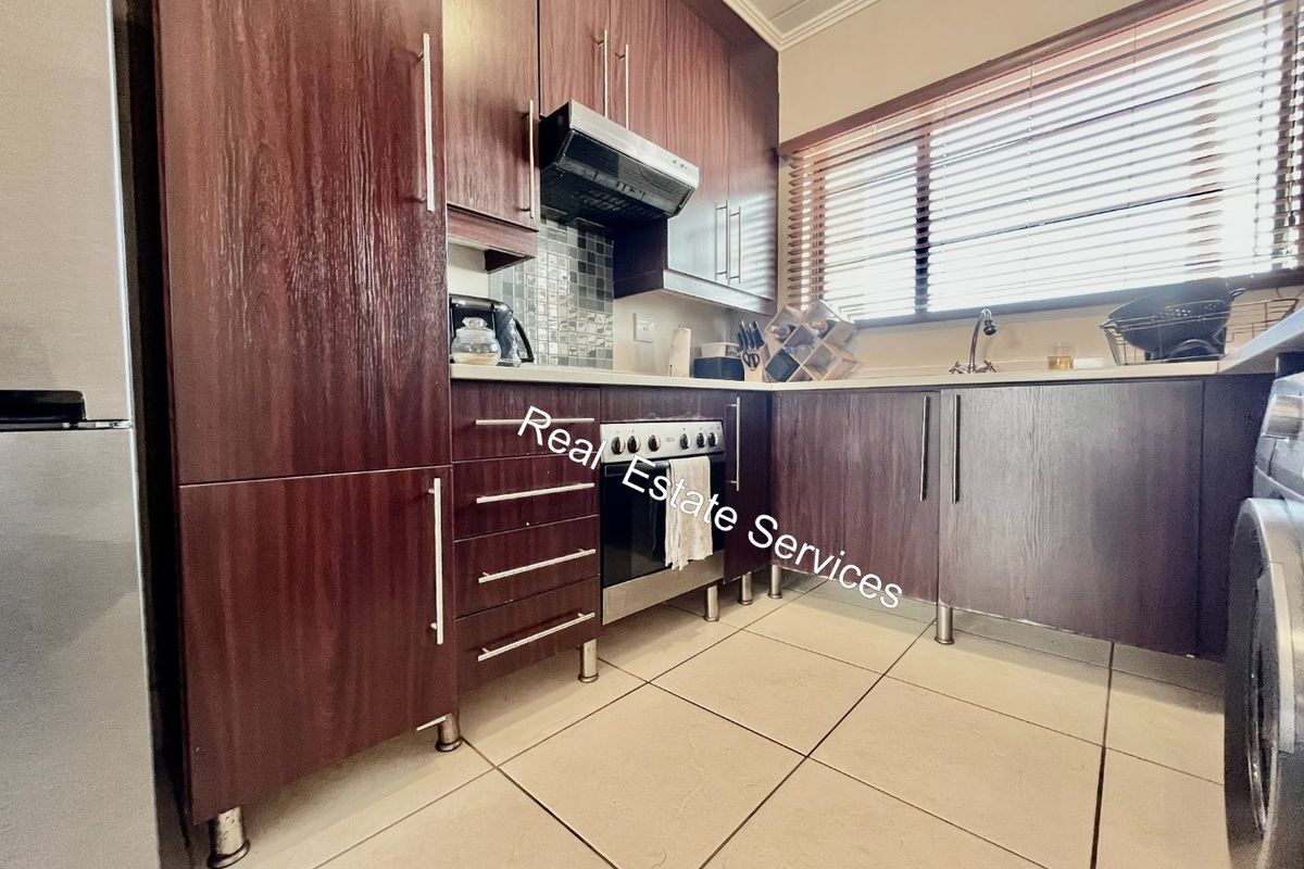 A functional kitchen featuring dark wood cabinetry, built-in oven, extractor fan, mosaic backsplash, and tiled flooring with natural light from the window.
