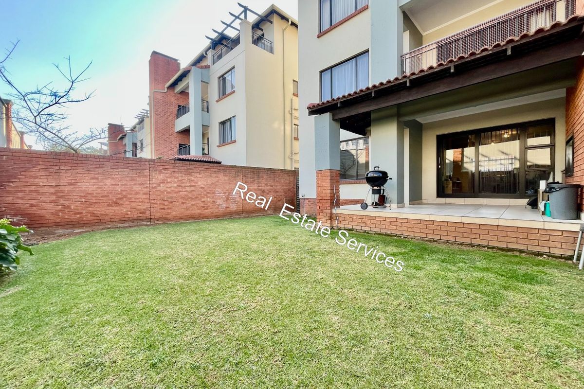 A private rear garden featuring a paved patio area, brick boundary wall, and direct access to the apartment via sliding glass doors.