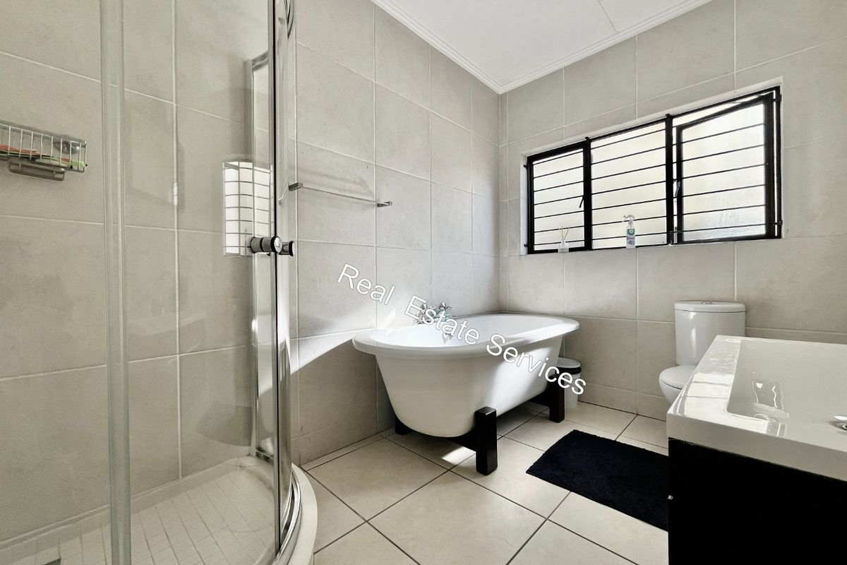 Modern bathroom featuring a freestanding bathtub, a separate curved glass shower enclosure, a vanity basin, and neutral floor-to-ceiling tiling.