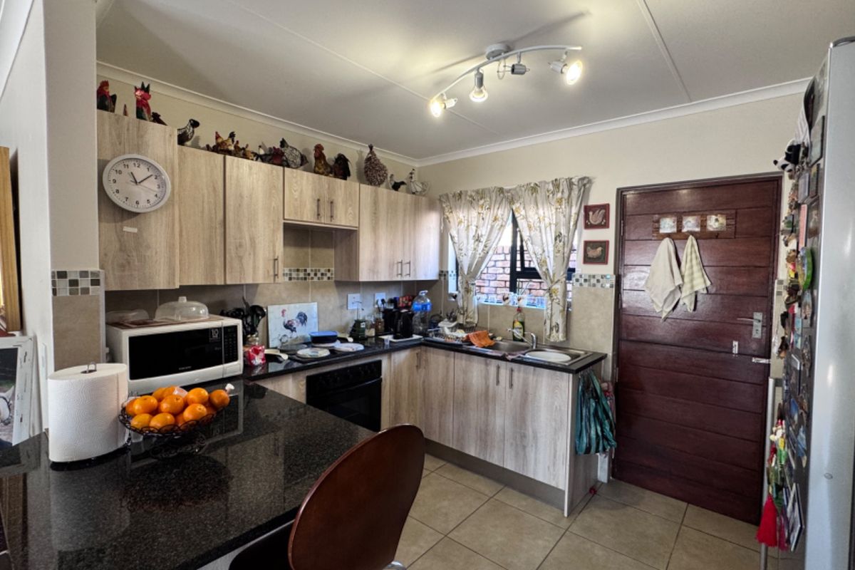 Functional kitchen featuring light wood-look cabinetry, dark granite countertops, built-in oven, hob, and tiled flooring with direct access to an exterior door.