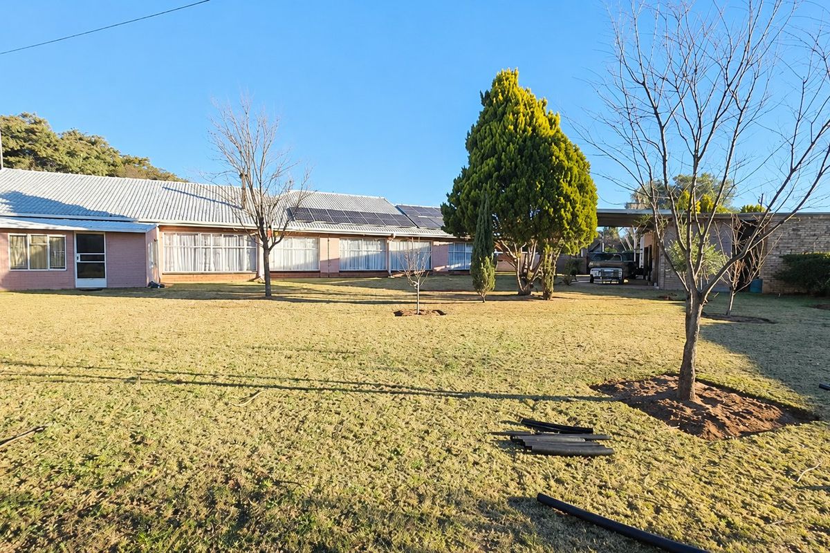 Rear view of the property featuring a large lawn, brick exterior, metal roofing, and integrated solar panels with an adjacent carport.