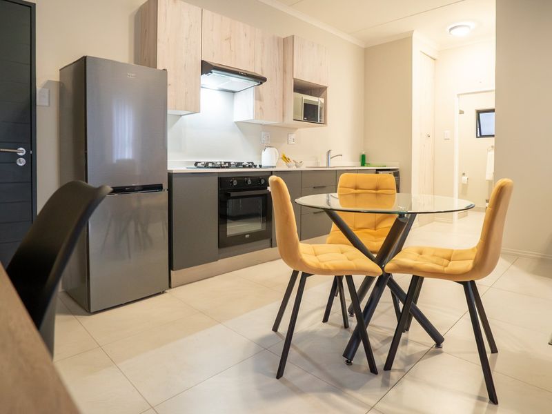 Modern open-plan kitchen and dining area featuring contemporary cabinetry, integrated appliances, and neutral tiled flooring, creating a functional and cohesive living space.