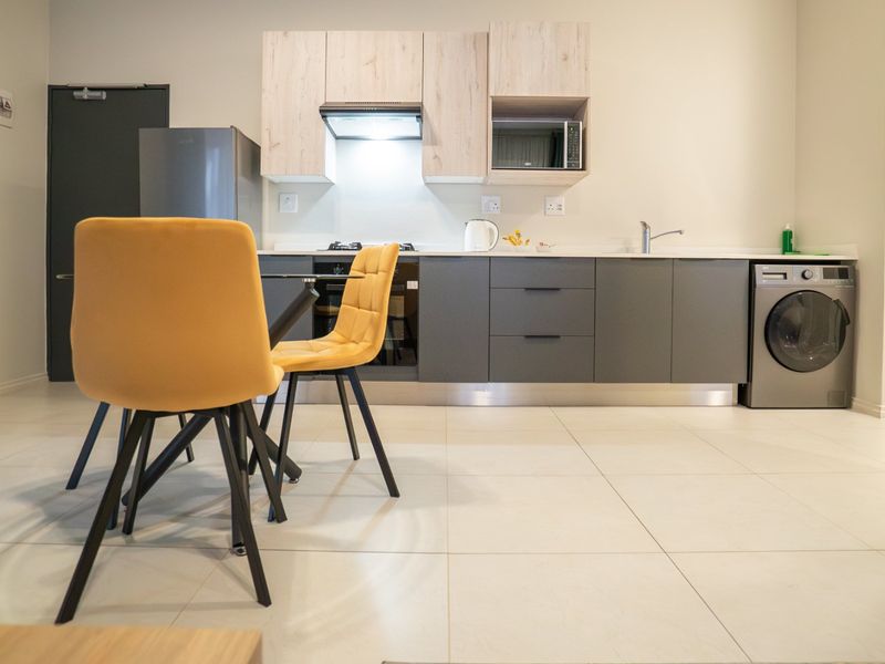 Modern open-plan kitchen featuring sleek grey and light wood cabinetry, integrated appliances, and neutral tiled flooring, seamlessly connecting to the living area.