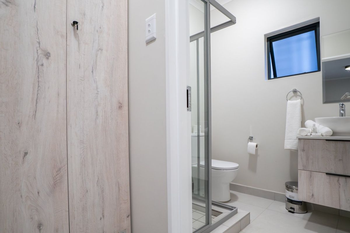 Modern bathroom featuring a vanity with basin, a glass-enclosed shower, a toilet, and light wood-look cabinetry.