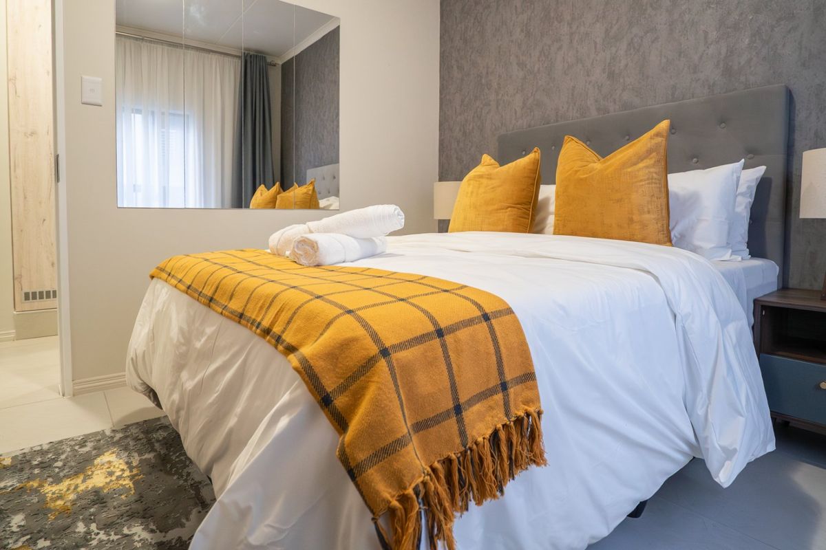 A well-maintained bedroom featuring a textured accent wall, tiled flooring, and a large wall-mounted mirror, creating a bright and comfortable living space.