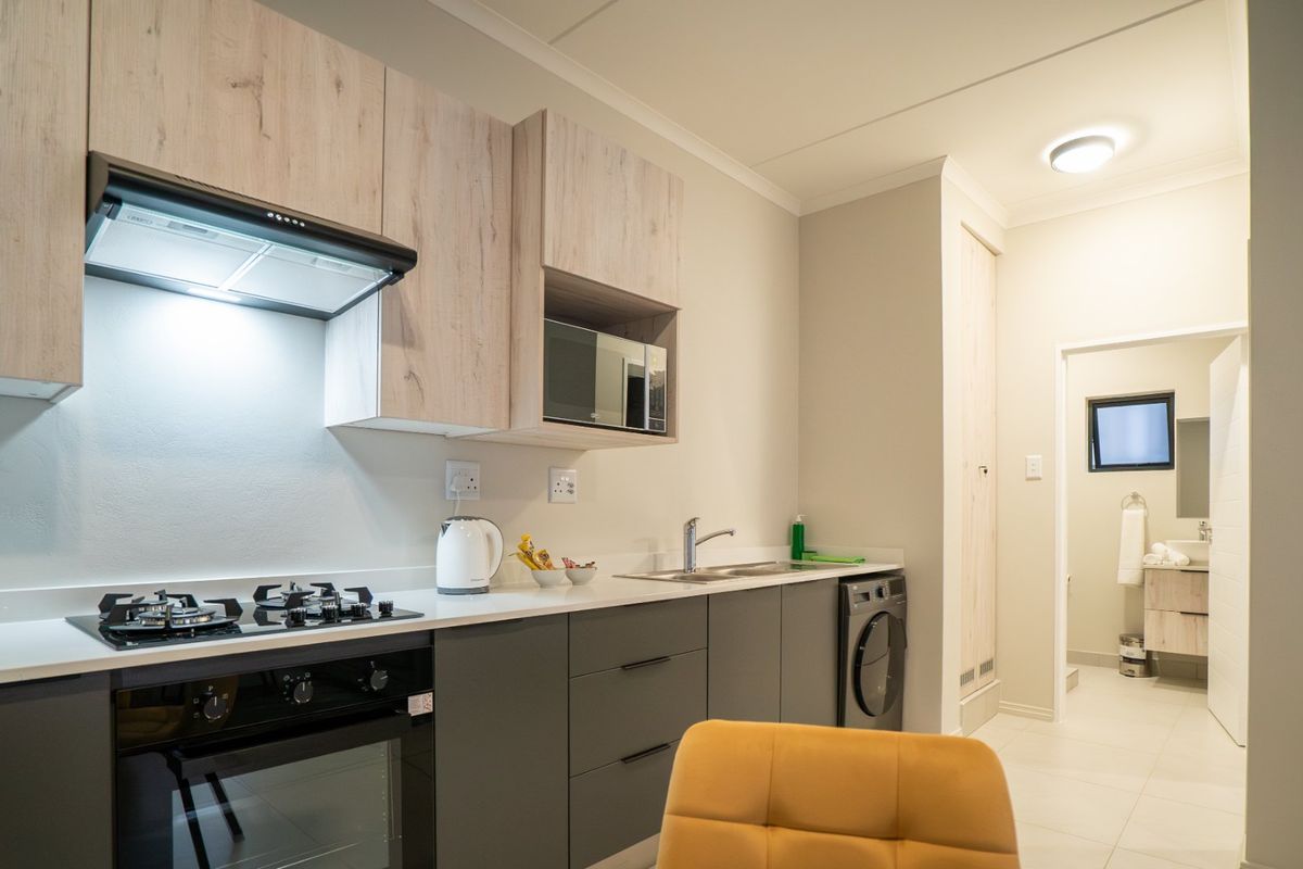 Modern kitchen featuring light wood-tone upper cabinets, dark grey lower cabinetry, stone countertops, integrated appliances, and a gas hob with extractor fan.