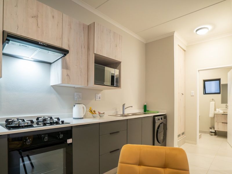 Modern kitchen featuring light wood-tone upper cabinets, dark grey lower cabinetry, stone countertops, integrated appliances, and a gas hob with extractor fan.