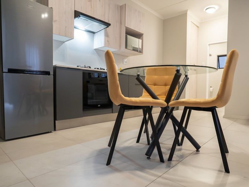 Modern open-plan kitchen featuring sleek cabinetry, integrated appliances, and light-toned tiled flooring, seamlessly flowing into the dining area.