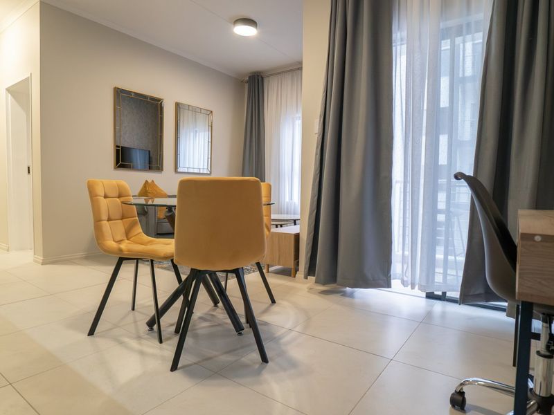 A bright open-plan living area featuring neutral tiled flooring, modern recessed lighting, and a large sliding glass door providing access to the balcony.