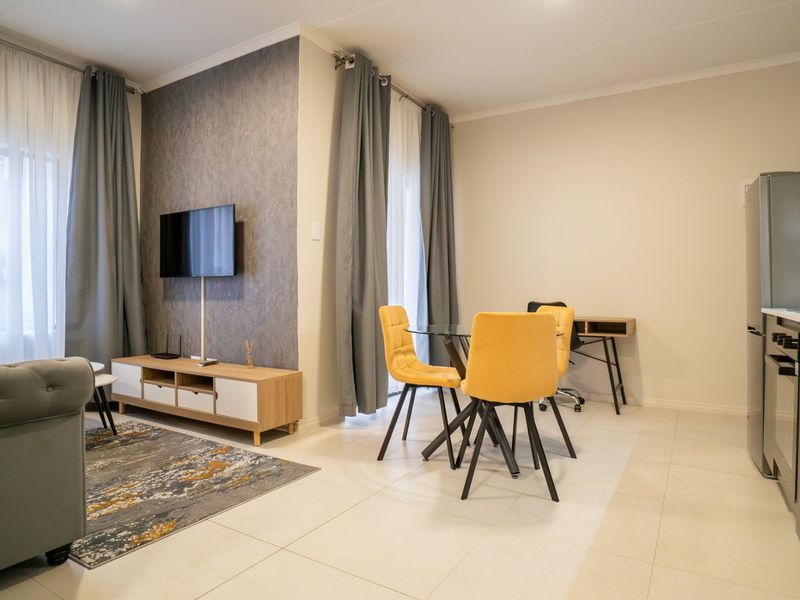 Modern open-plan living area featuring a sleek kitchen with built-in appliances, tiled flooring, and a stylish feature wall.