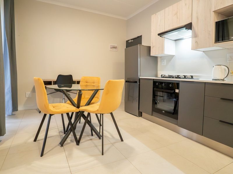 Modern open-plan kitchen and dining area featuring sleek grey cabinetry, built-in appliances, and light-toned tiled flooring.