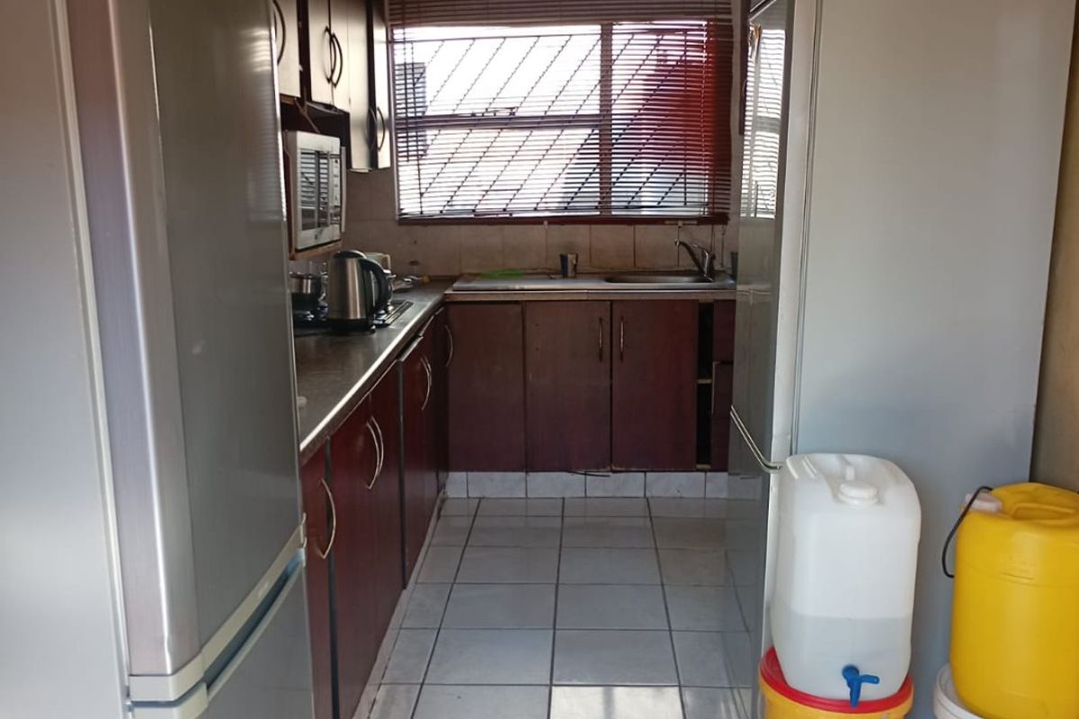 A functional galley-style kitchen featuring dark wood-tone cabinetry, tiled flooring, and a stainless steel sink, offering potential for a modern renovation.