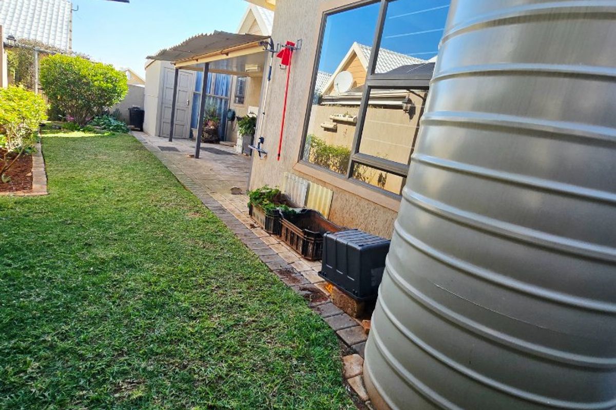 A view of the rear garden featuring a paved patio area, lawn, and a large water storage tank against the exterior wall.