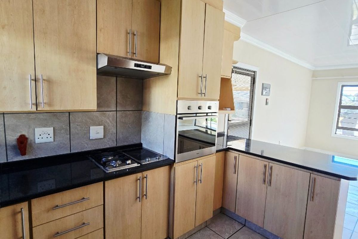 A functional kitchen featuring light wood cabinetry, black granite countertops, a gas hob, built-in oven, and tiled flooring.