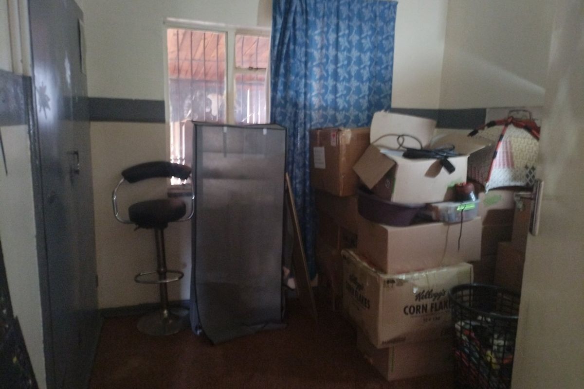 A bedroom featuring a window with security bars and a built-in cupboard, currently used for storage.