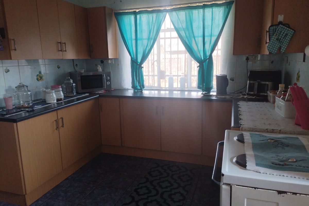 A functional kitchen featuring laminate cabinetry, dark countertops, tiled backsplash, and tiled flooring with security bars installed on the window.