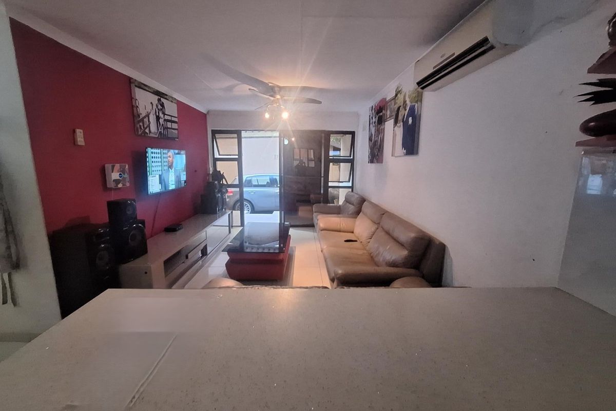 A living room featuring tiled flooring, a ceiling fan, and a wall-mounted air conditioning unit, with direct access to an outdoor area via sliding doors.
