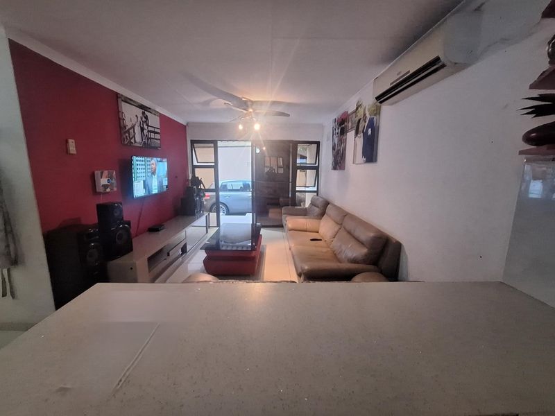 A living room featuring tiled flooring, a ceiling fan, and a wall-mounted air conditioning unit, with direct access to an outdoor area via sliding doors.