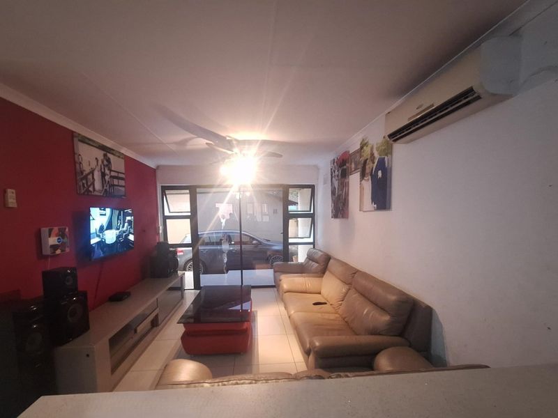 A living room featuring tiled floors, a ceiling fan, and a wall-mounted air conditioning unit, with direct access to an outdoor area via sliding doors.