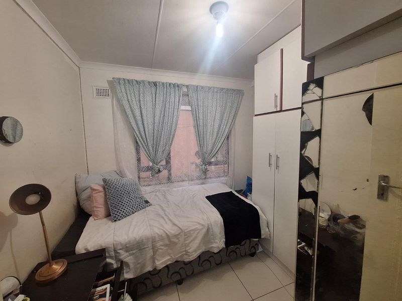 A compact bedroom featuring built-in cupboards, tiled flooring, and a window with natural light. The room requires cosmetic updates to improve its overall condition.