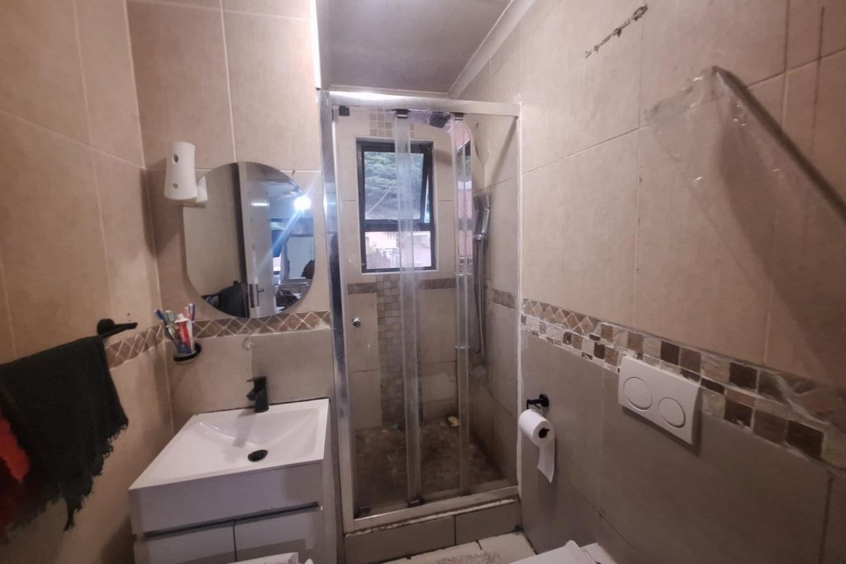 Compact bathroom featuring a shower enclosure, wall-mounted toilet, and a modern vanity basin with tiled finishes throughout.