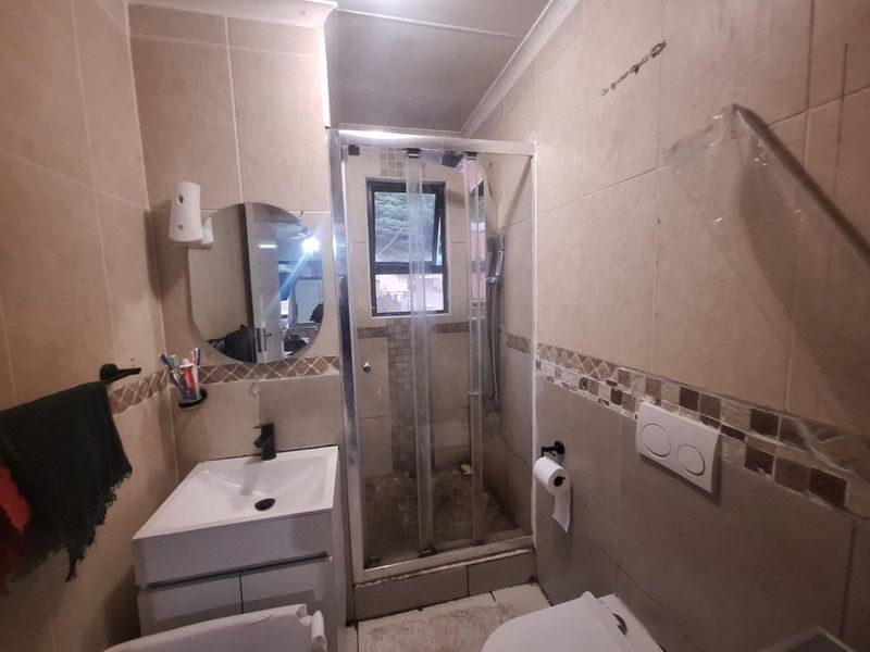 Compact bathroom featuring a shower enclosure, wall-mounted toilet, and a modern vanity basin with tiled finishes throughout.