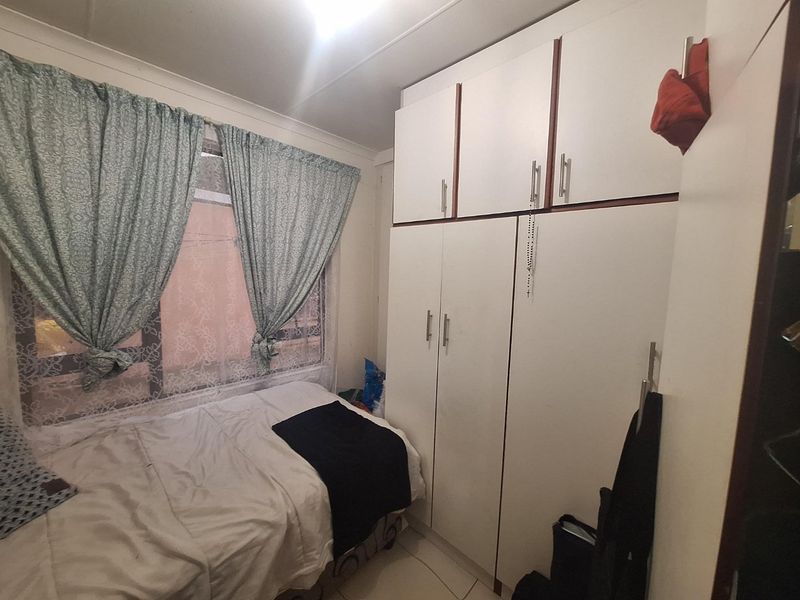 A compact bedroom featuring white built-in cupboards with overhead storage and tiled flooring.