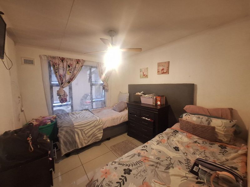 A bedroom featuring tiled flooring and a ceiling fan, currently showing signs of wear on the walls.
