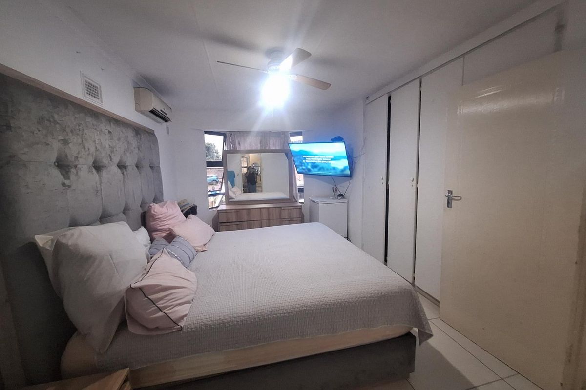 A functional bedroom featuring built-in cupboards, a ceiling fan, and an air conditioning unit, finished with tiled flooring.