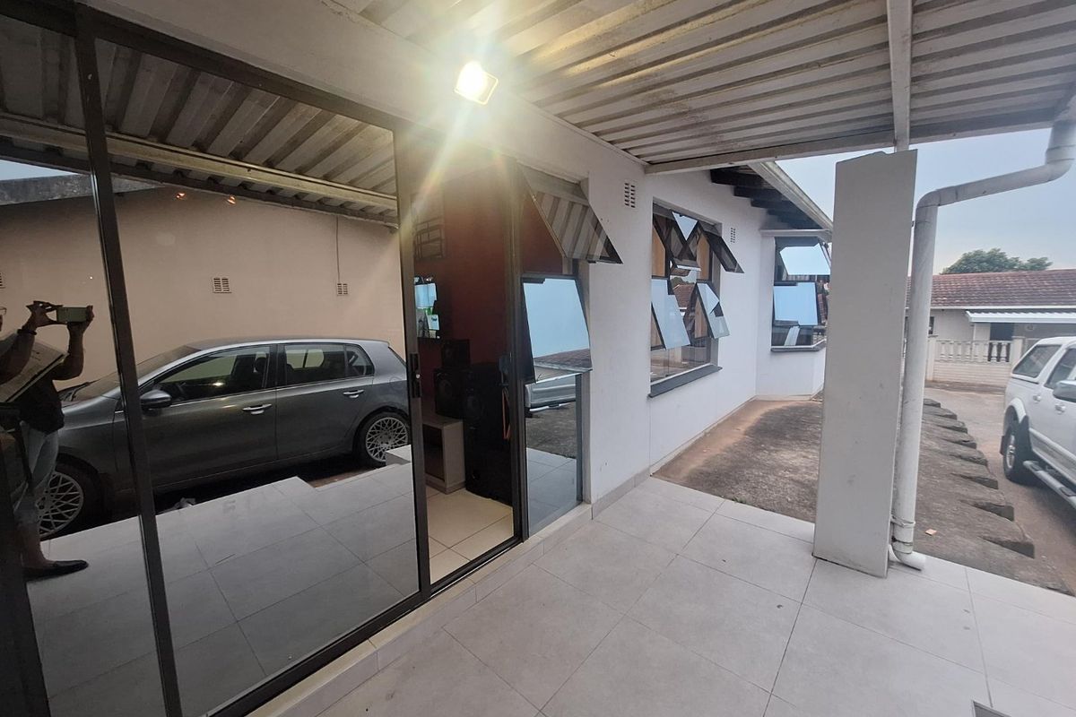 A covered patio area featuring tiled flooring, sliding glass doors, and a corrugated metal roof, providing a functional outdoor transition space.