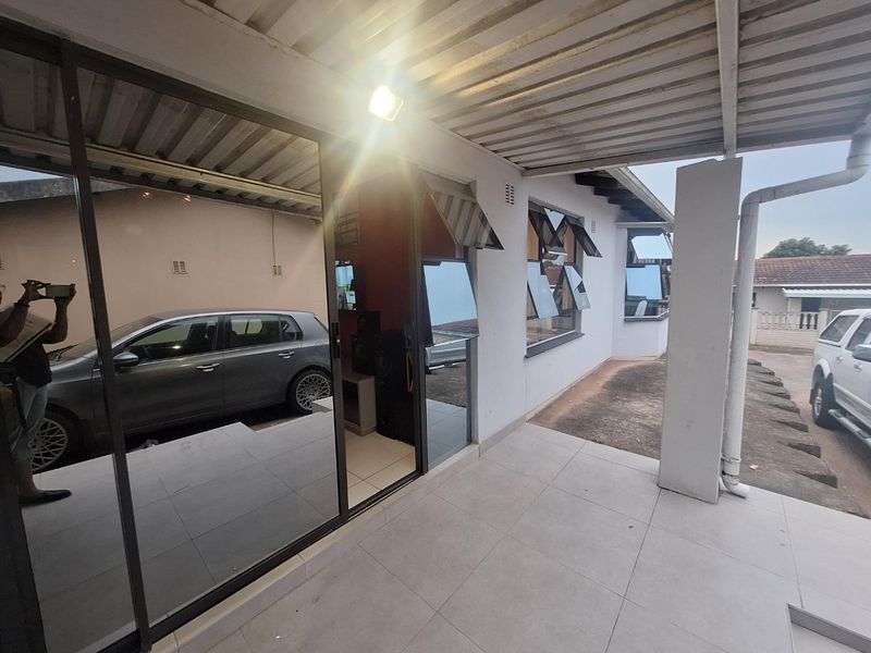 A covered patio area featuring tiled flooring, sliding glass doors, and a corrugated metal roof, providing a functional outdoor transition space.